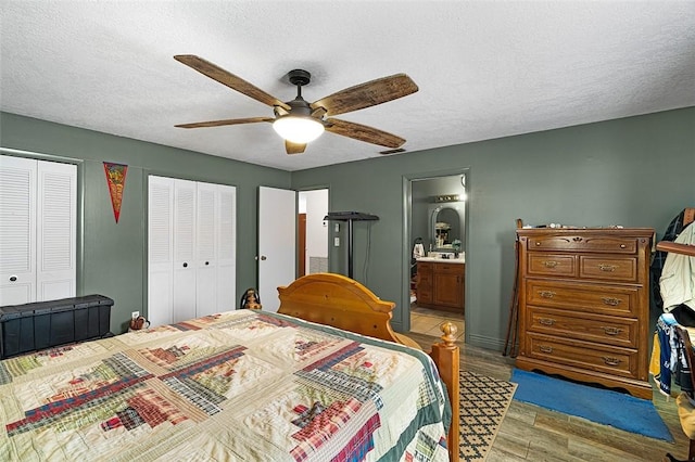 bedroom featuring ensuite bathroom, a textured ceiling, light wood finished floors, and two closets