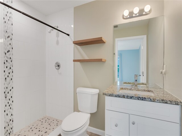 bathroom featuring a tile shower, vanity, and toilet