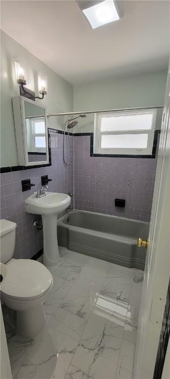 bathroom with toilet, tile walls, and tiled shower / bath