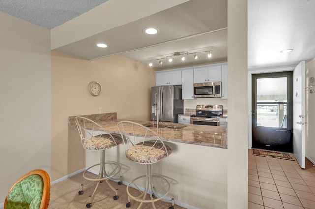 kitchen with a breakfast bar, white cabinets, appliances with stainless steel finishes, light tile patterned flooring, and kitchen peninsula