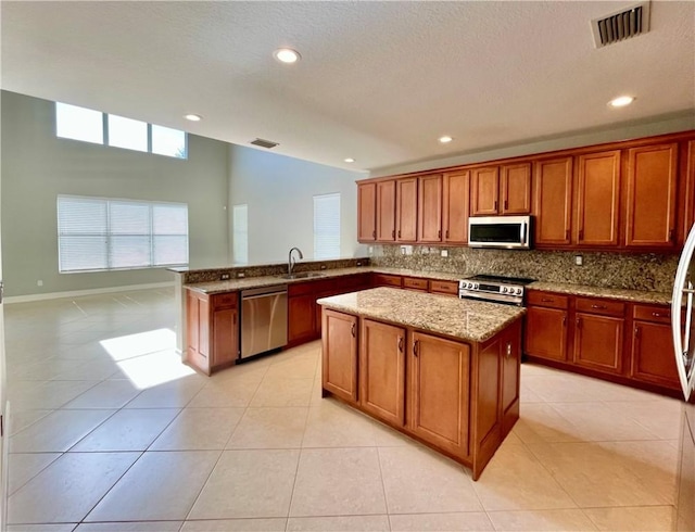 kitchen featuring light stone countertops, sink, tasteful backsplash, kitchen peninsula, and appliances with stainless steel finishes