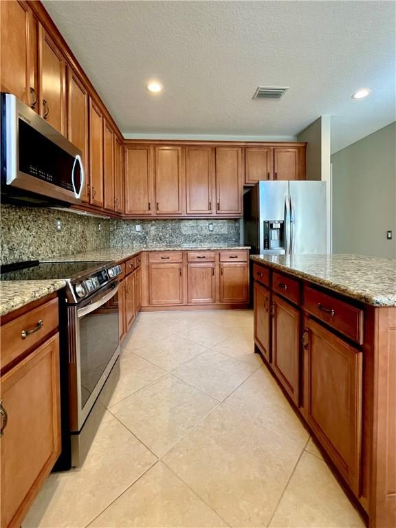 kitchen featuring backsplash, light stone countertops, stainless steel appliances, and light tile patterned floors