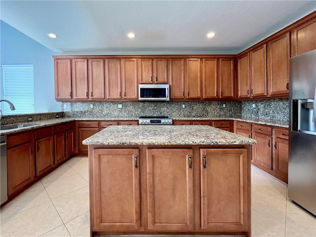 kitchen featuring light stone countertops, backsplash, stainless steel appliances, sink, and a center island