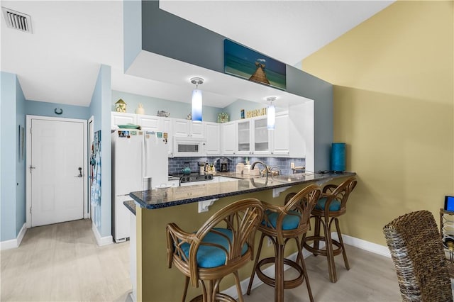 223 River Walk Unit 12, Hutchinson Island, FL 34949 - kitchen featuring white appliances, a peninsula, backsplash, white cabinetry, and dark stone counters