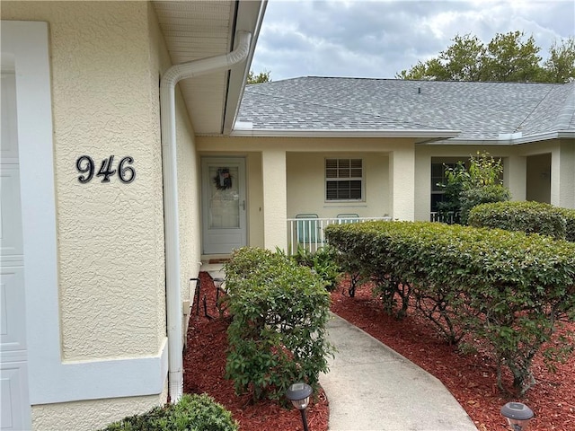 view of exterior entry featuring a shingled roof, an attached garage, cooling unit, and stucco siding