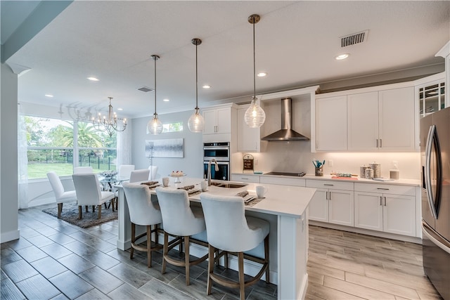 kitchen featuring white cabinetry, wall chimney exhaust hood, light hardwood / wood-style floors, pendant lighting, and appliances with stainless steel finishes