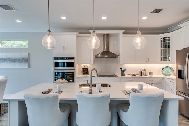 kitchen featuring wall chimney exhaust hood, stainless steel appliances, sink, white cabinetry, and hanging light fixtures