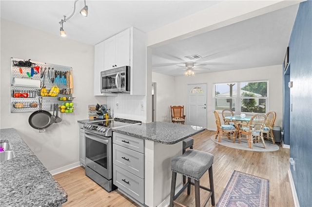 2106 36th Ave, Vero Beach, FL 32960 - kitchen with stainless steel appliances, a breakfast bar area, light stone countertops, a peninsula, and light wood-style flooring