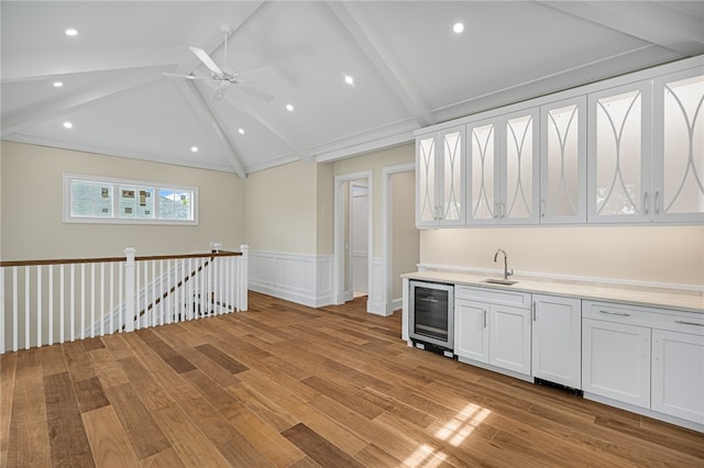 kitchen with white cabinetry, wine cooler, sink, vaulted ceiling with beams, and light hardwood / wood-style flooring