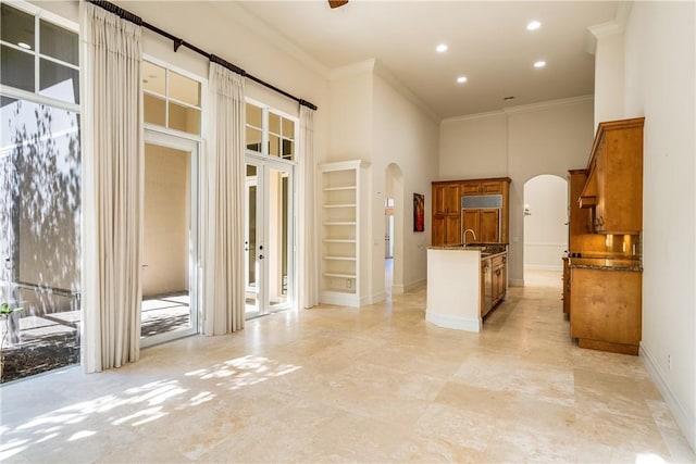 interior space featuring ornamental molding, a sink, arched walkways, baseboards, and a towering ceiling