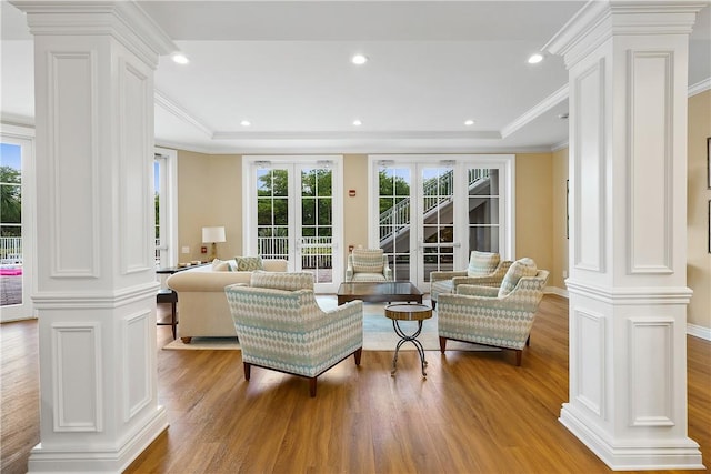 living area with a raised ceiling, ornate columns, and wood finished floors