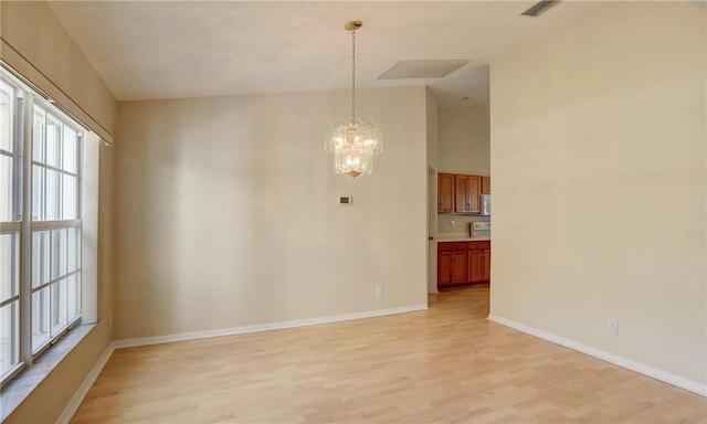unfurnished dining area featuring a notable chandelier, light wood-type flooring, and baseboards