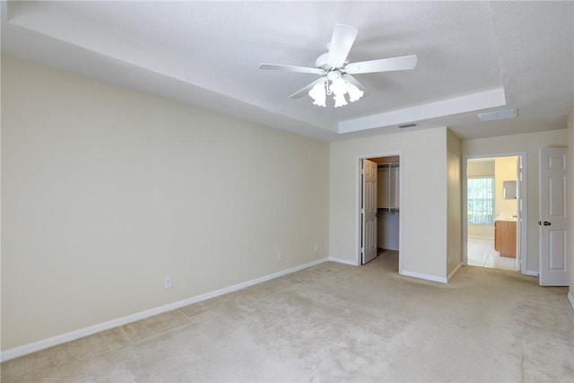 unfurnished bedroom featuring light colored carpet, baseboards, a raised ceiling, and ceiling fan