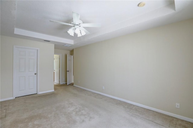 empty room featuring light colored carpet, a raised ceiling, baseboards, and a ceiling fan