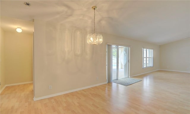 spare room featuring lofted ceiling, baseboards, light wood-style flooring, and a chandelier