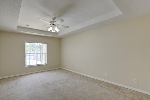 unfurnished room featuring a tray ceiling, carpet flooring, baseboards, and a ceiling fan