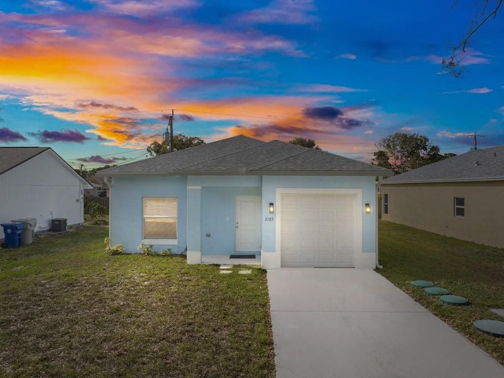 view of front of home with a lawn, a garage, and central AC