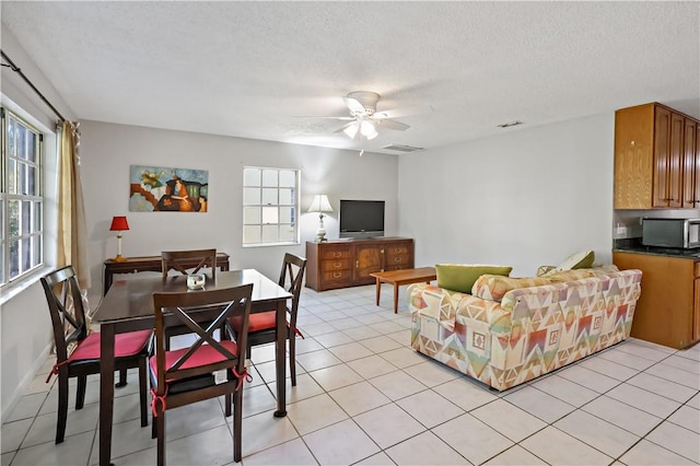 living area featuring visible vents, baseboards, ceiling fan, a textured ceiling, and light tile patterned floors