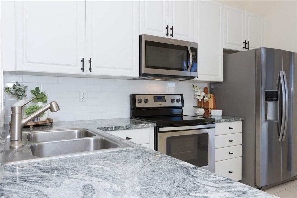 9926 E Villa Cir, Vero Beach, FL 32966 - kitchen featuring stainless steel appliances, a sink, white cabinets, decorative backsplash, and light stone counters