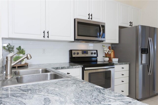 kitchen with a sink, light stone counters, white cabinetry, appliances with stainless steel finishes, and decorative backsplash