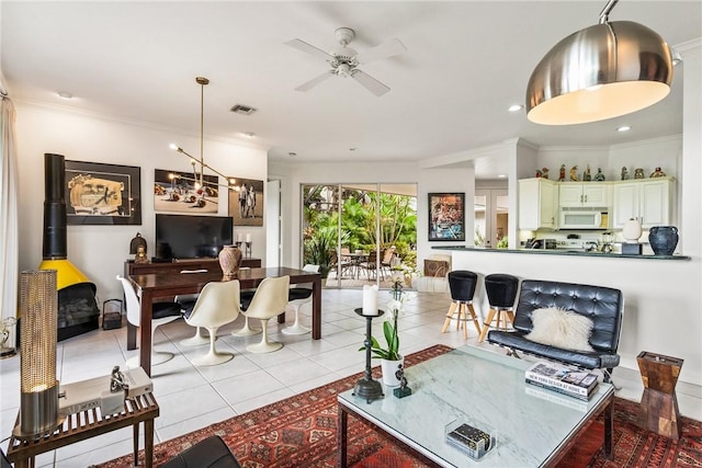 living room featuring a wood stove, crown molding, light tile patterned flooring, and ceiling fan with notable chandelier