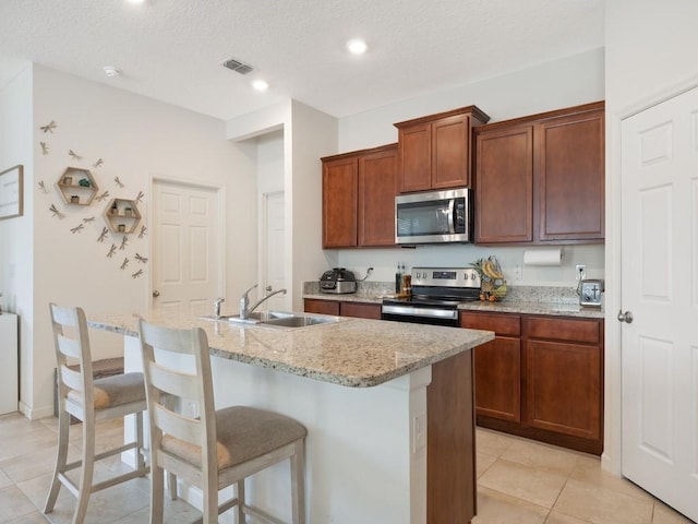 kitchen with an island with sink, light stone counters, appliances with stainless steel finishes, a kitchen breakfast bar, and a sink