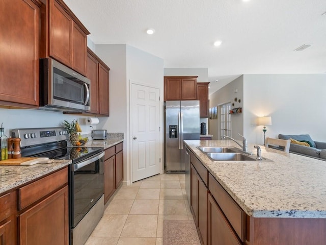 kitchen featuring visible vents, light stone countertops, a center island with sink, appliances with stainless steel finishes, and a sink