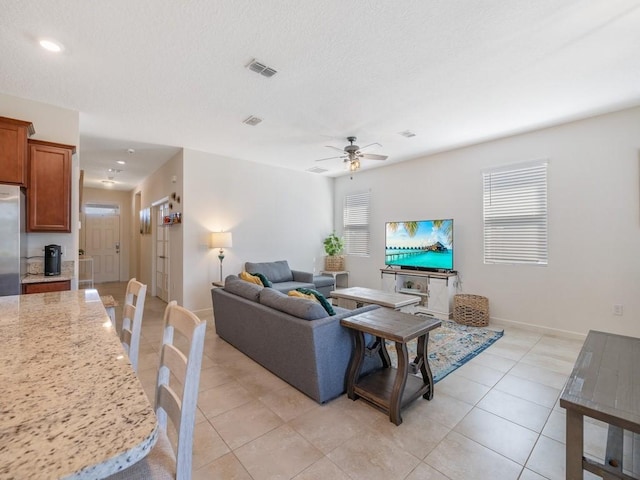 living room featuring light tile patterned floors, a ceiling fan, visible vents, and a textured ceiling