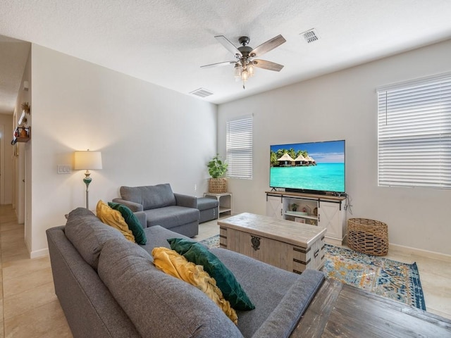 living area with baseboards, a ceiling fan, visible vents, and a textured ceiling