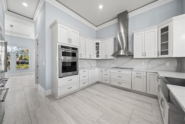 kitchen featuring wall chimney range hood, double oven, white cabinets, black electric cooktop, and decorative backsplash