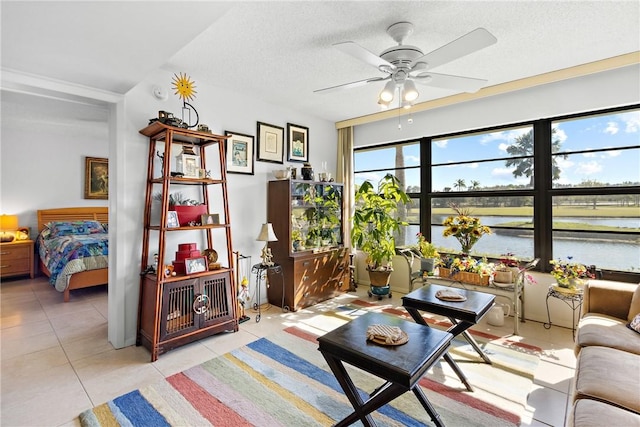 tiled living room with ceiling fan, a water view, and a textured ceiling