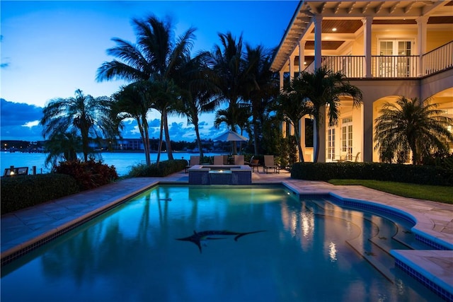 view of pool with french doors, a water view, a pool with connected hot tub, and a patio area