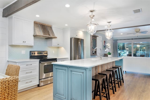 kitchen with stainless steel appliances, custom range hood, a center island with sink, and white cabinetry