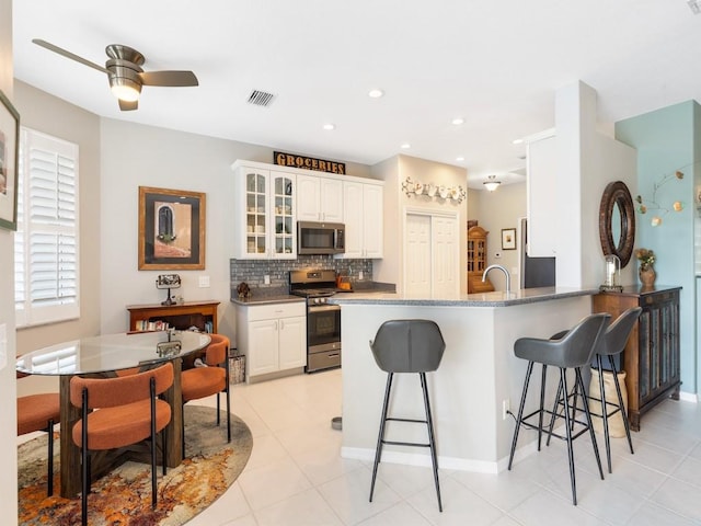 kitchen featuring a kitchen bar, kitchen peninsula, white cabinets, and appliances with stainless steel finishes