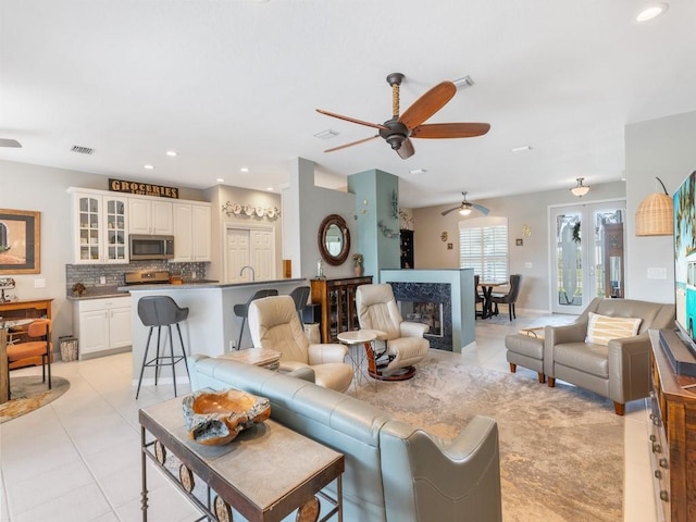 tiled living room featuring a fireplace, french doors, and ceiling fan