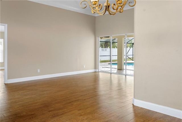 empty room with a chandelier, wood-type flooring, and a towering ceiling