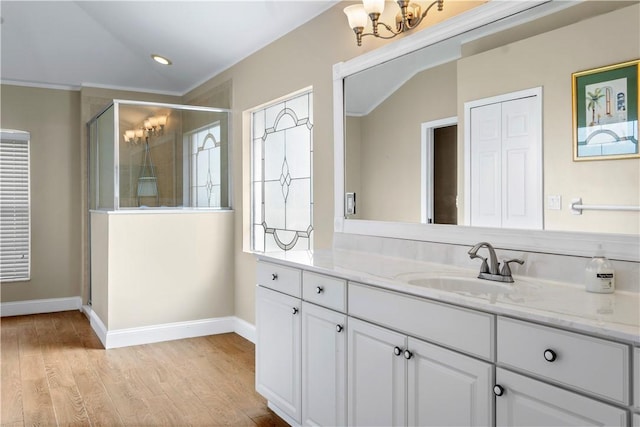 bathroom featuring an inviting chandelier, wood-type flooring, an enclosed shower, vanity, and ornamental molding