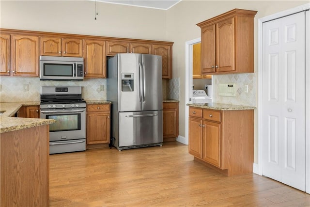 kitchen featuring washing machine and dryer, decorative backsplash, light hardwood / wood-style flooring, and appliances with stainless steel finishes