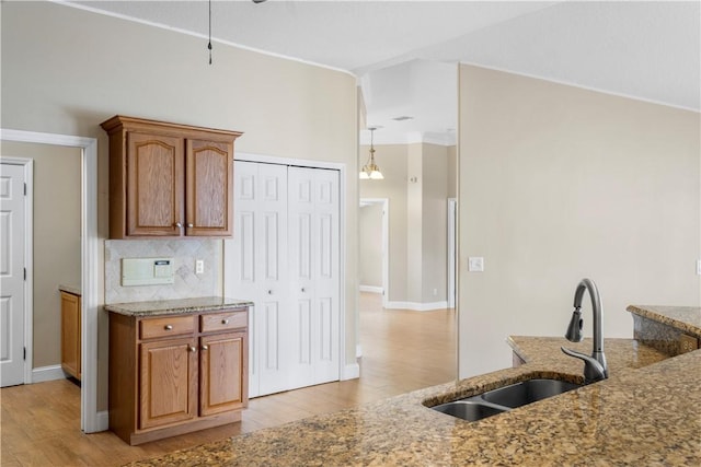 kitchen featuring decorative backsplash, light wood-type flooring, light stone counters, and sink