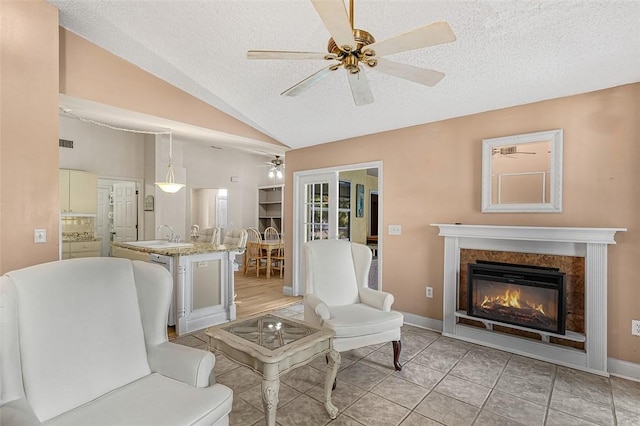 living area featuring lofted ceiling, a textured ceiling, light tile patterned flooring, a fireplace, and a ceiling fan