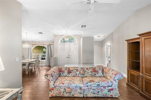 living area with a textured ceiling, dark wood finished floors, visible vents, and baseboards