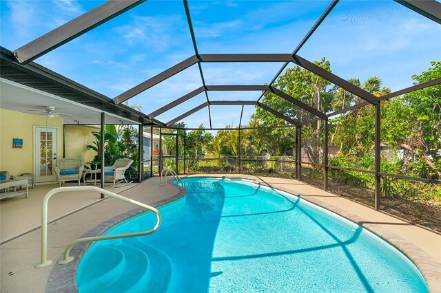 outdoor pool with glass enclosure, a patio area, and a ceiling fan