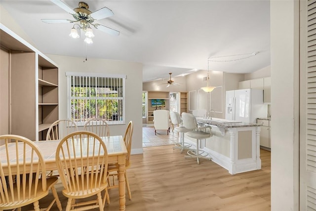 dining room featuring light wood-style floors, vaulted ceiling, and a ceiling fan