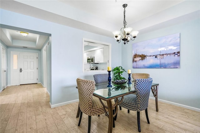 5520 N Harbor Village Dr Unit 204, Vero Beach, FL 32967 - dining space featuring a tray ceiling, light wood-style flooring, a chandelier, and baseboards