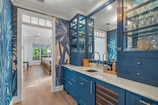 bar with blue cabinetry, sink, ornamental molding, and light wood-type flooring