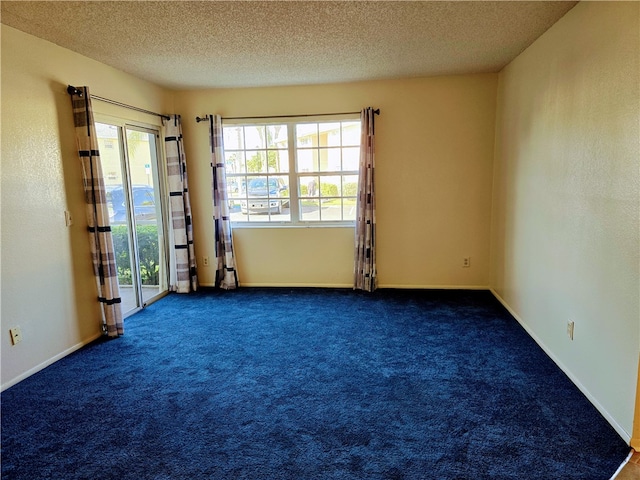 empty room with a textured ceiling, dark carpet, and plenty of natural light