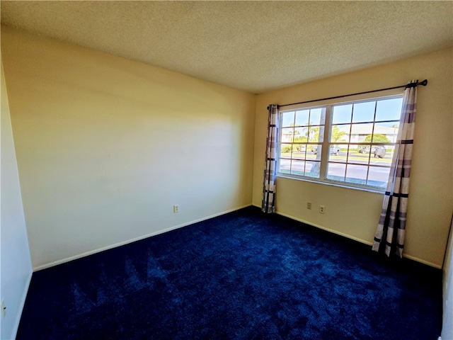 spare room with a textured ceiling and dark carpet