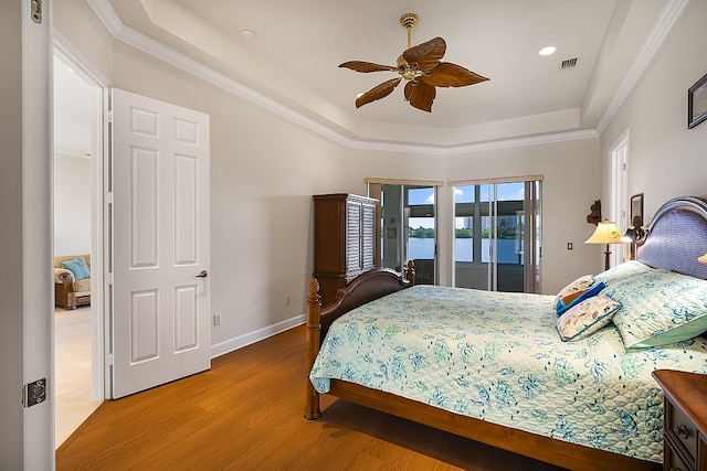 bedroom with a tray ceiling, hardwood / wood-style floors, ceiling fan, and access to exterior