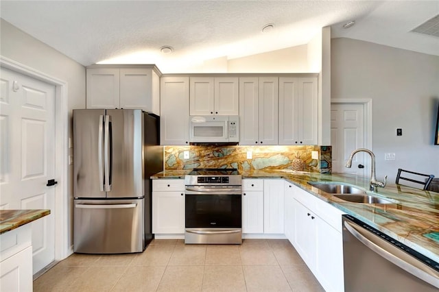 kitchen featuring tasteful backsplash, stainless steel appliances, lofted ceiling, light tile patterned floors, and sink