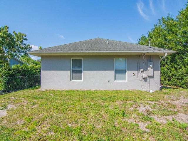 back of house featuring stucco siding, a lawn, roof with shingles, and fence